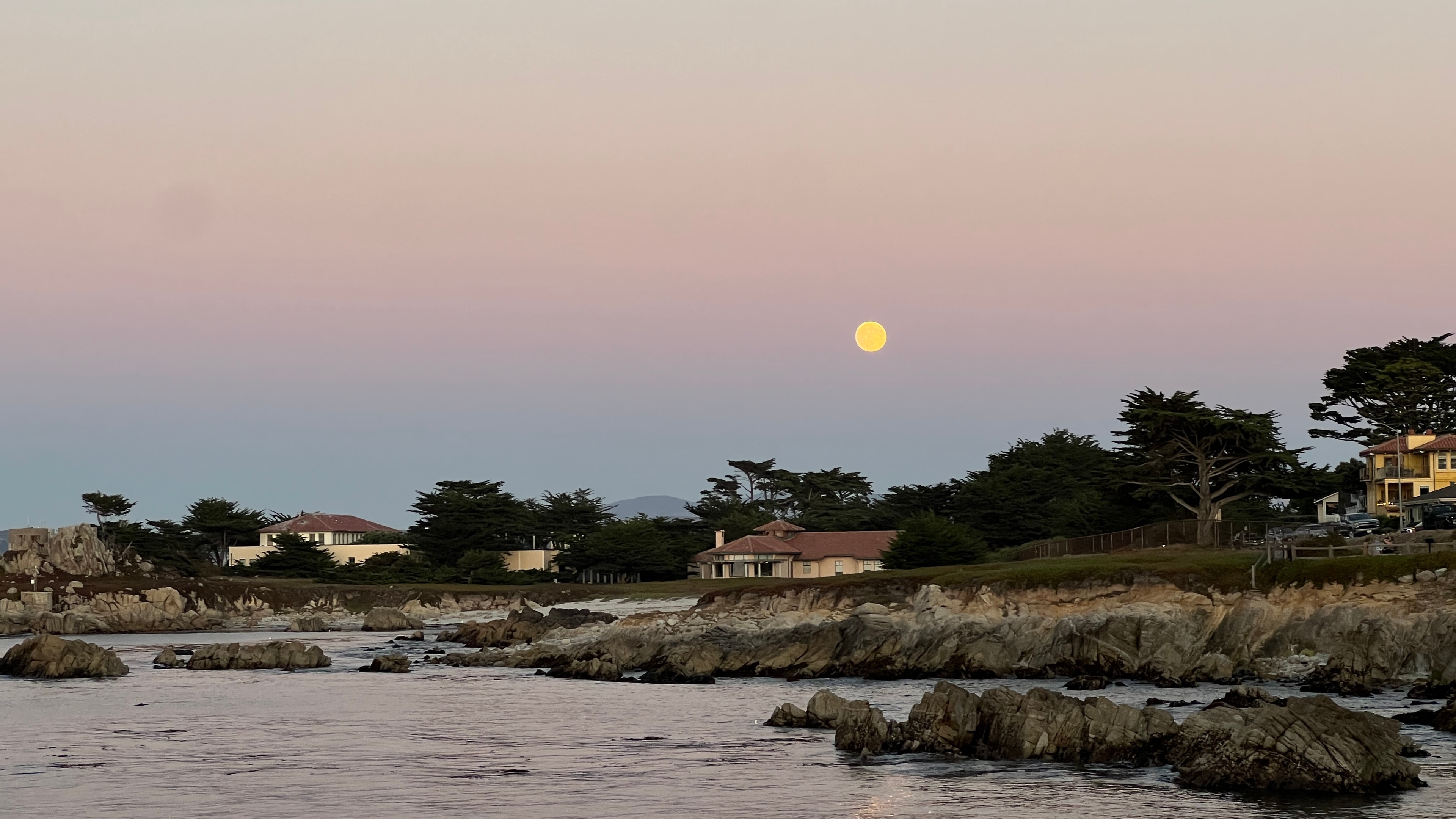 A full moon rising over a rocky coastline at dusk